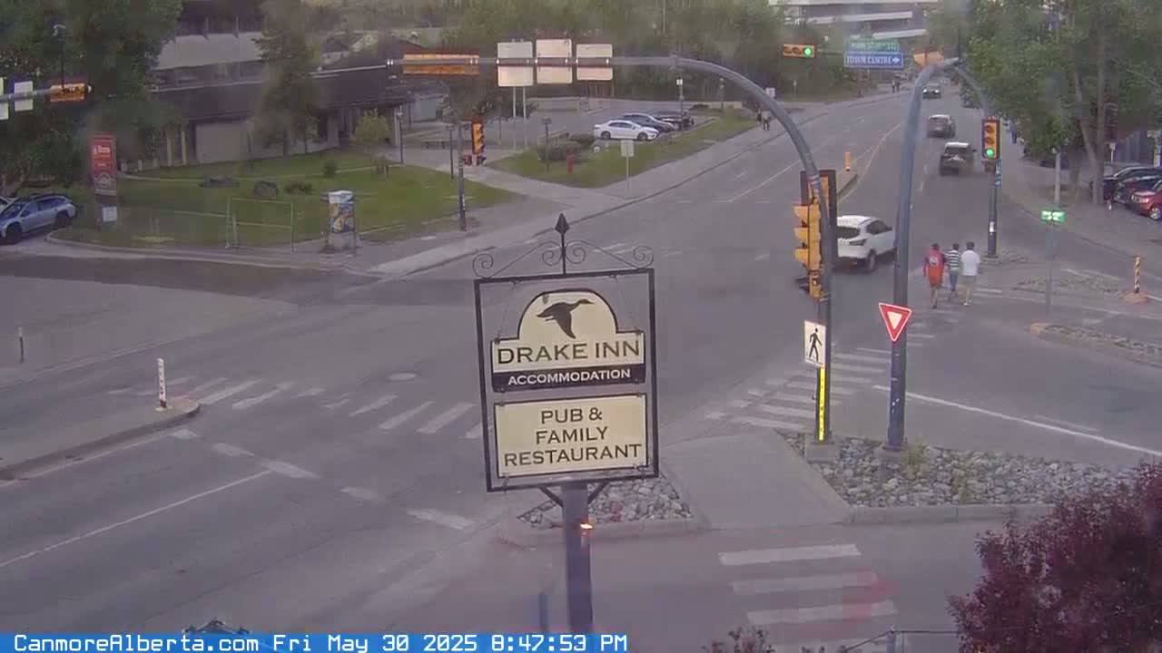 A street intersection with a Drake Inn pub and family restaurant sign, cars, and pedestrians, under overcast conditions.