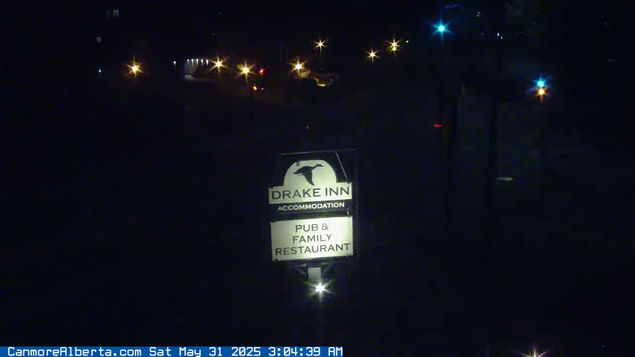 A nighttime view of a Drake Inn sign illuminated by a light below it, with distant lights visible in the background.