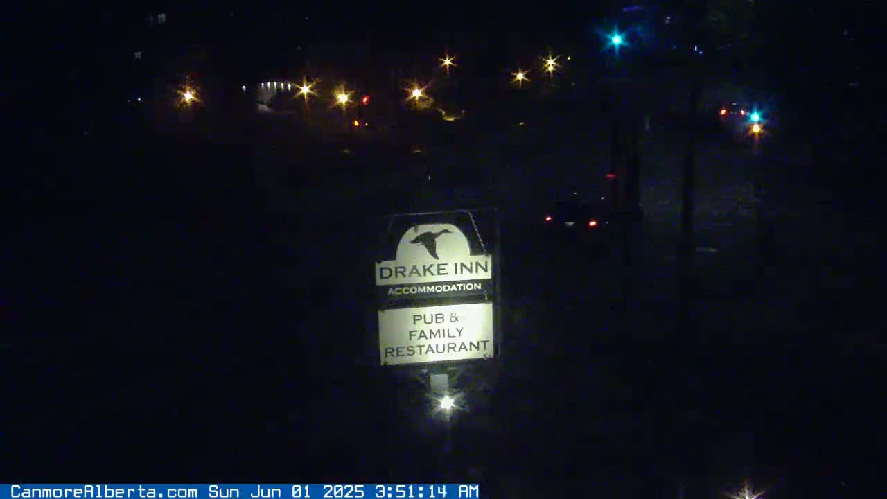 A nighttime view of a Drake Inn sign, illuminated by streetlights and vehicle headlights, in the distance.