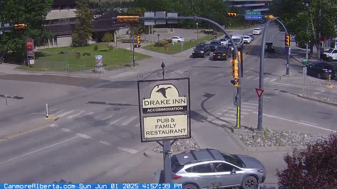 A sunny day shows a street intersection with several cars, a Drake Inn sign, and green trees in the background.