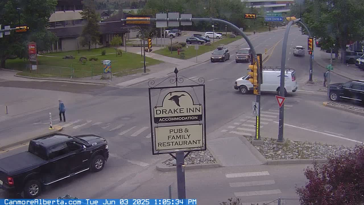 A street intersection with several vehicles, a pedestrian crossing, and a Drake Inn sign, on an overcast day.