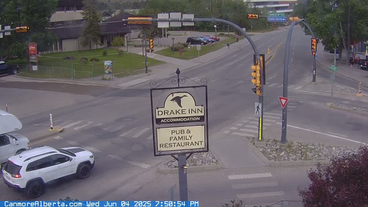 A partly cloudy daytime view of a street intersection with a Drake Inn pub and family restaurant sign, traffic lights, and a white Jeep parked nearby.