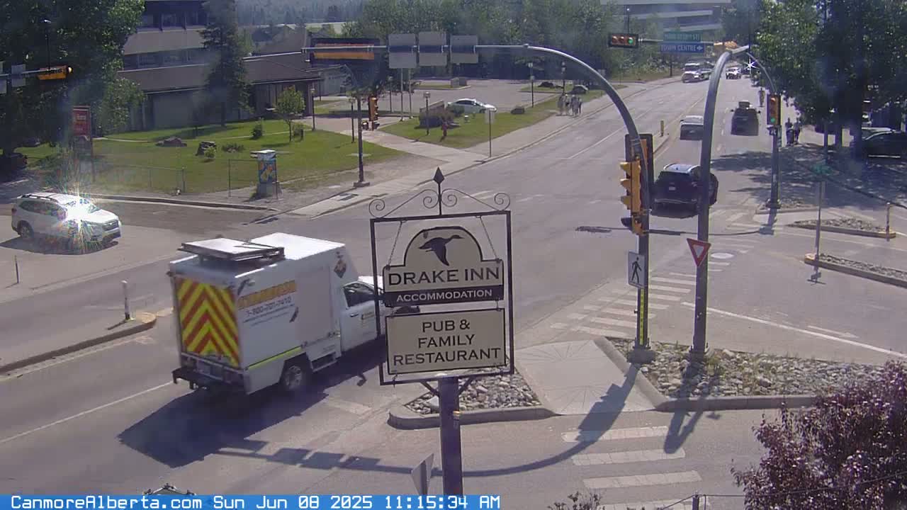 A sunny street intersection with several vehicles, a Drake Inn sign, and a service truck.