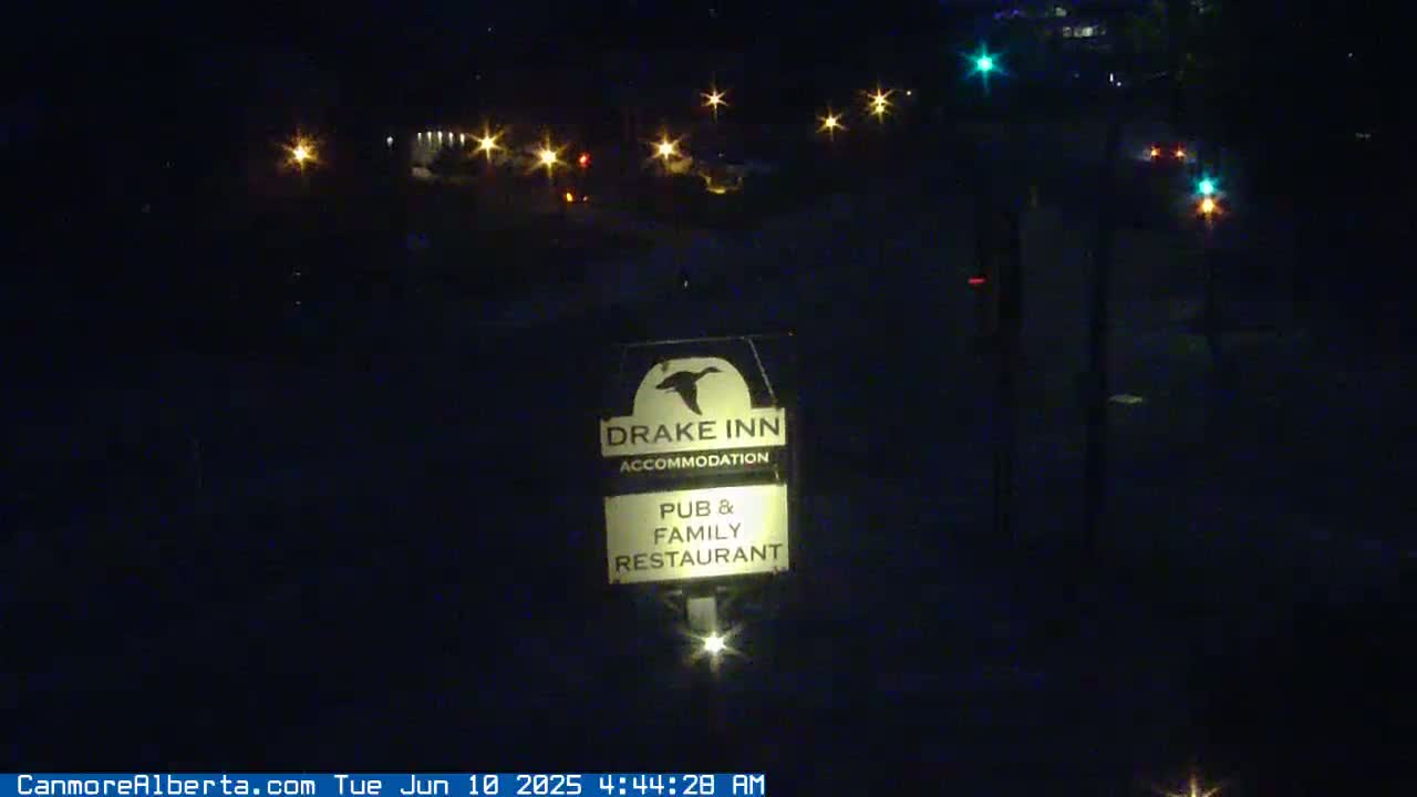 A nighttime view shows a Drake Inn sign illuminated in front of a dimly lit road with distant streetlights.