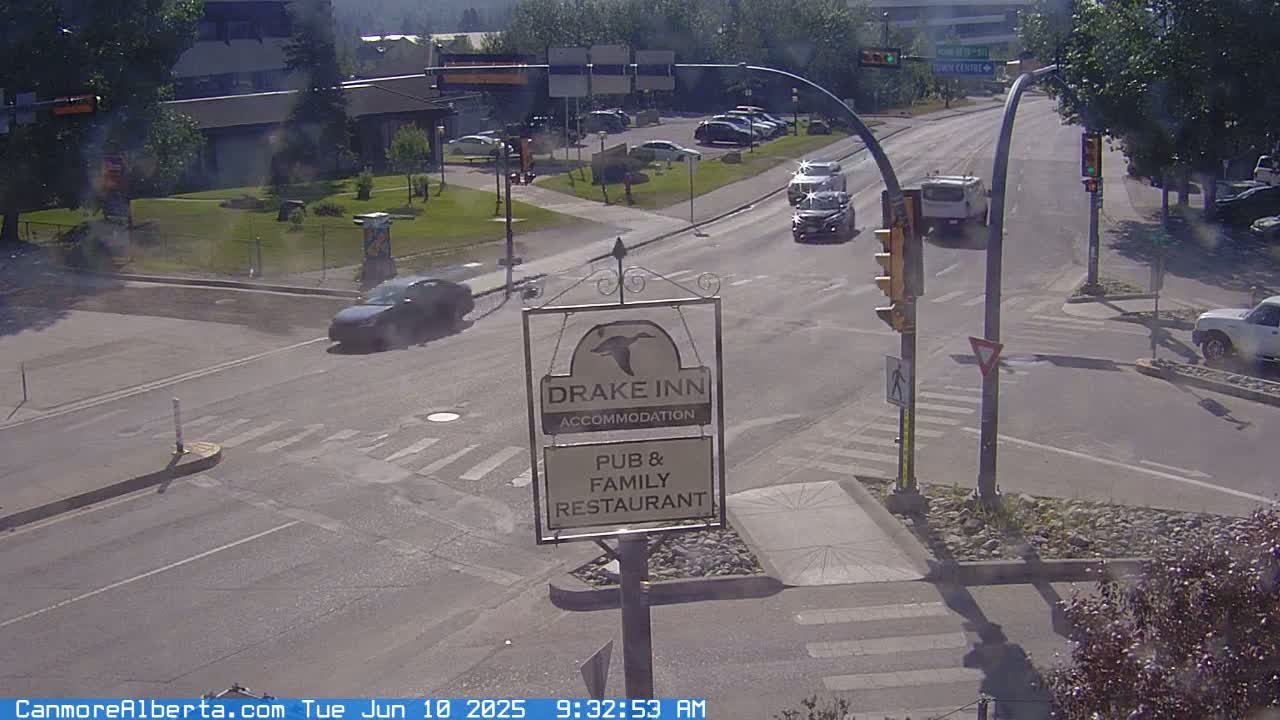 A sunny street intersection shows several cars at a stoplight near a Drake Inn sign.