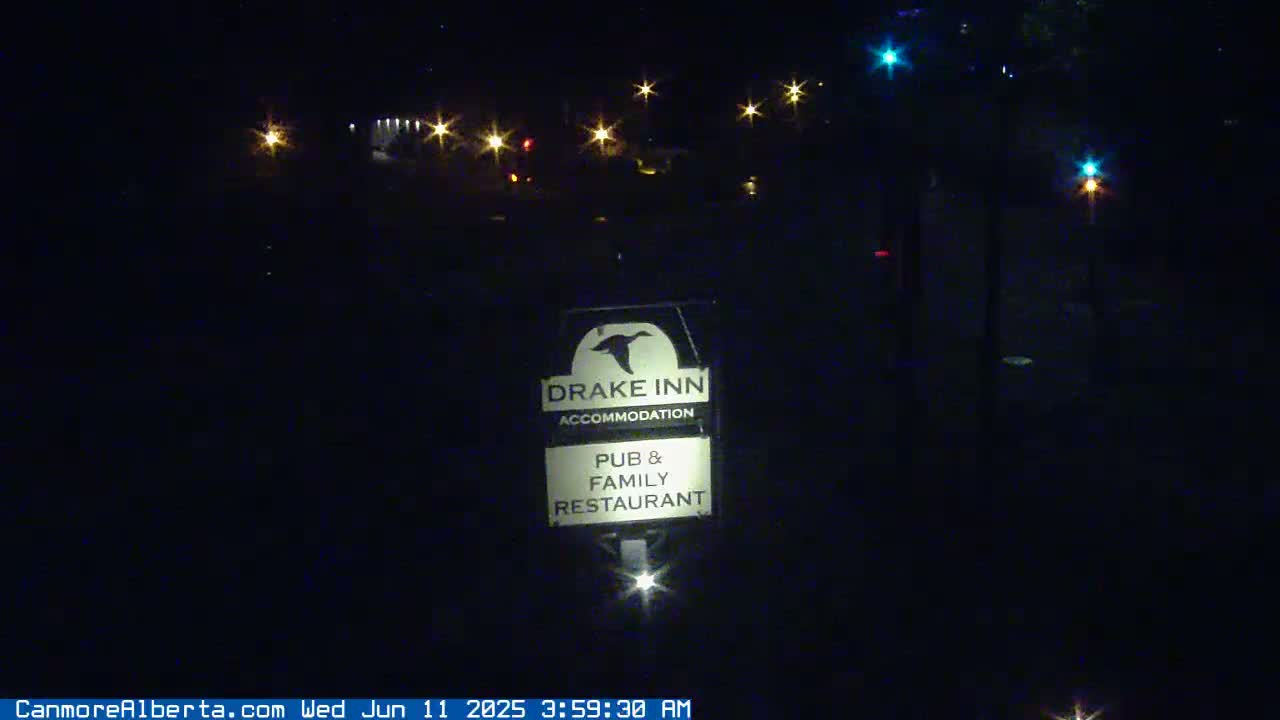 A nighttime view of a Drake Inn sign advertising accommodation, pub, and family restaurant, illuminated by several distant lights.