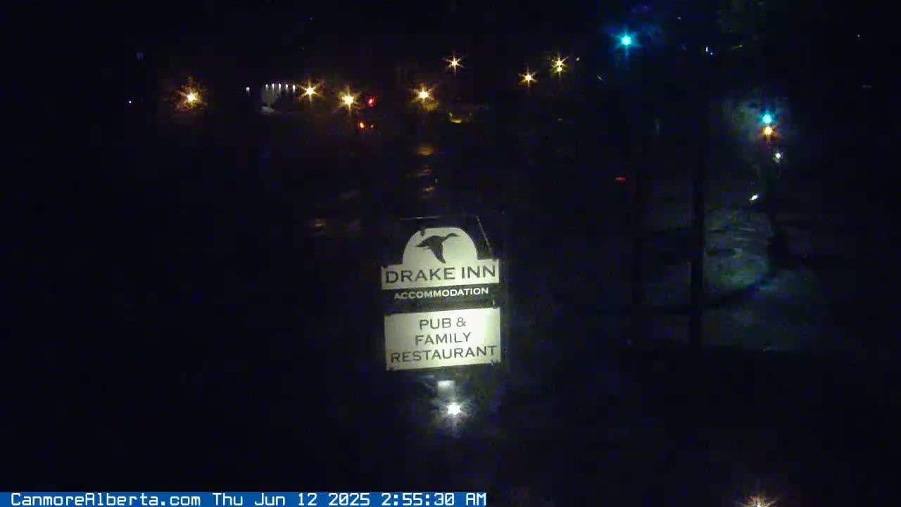 A nighttime, outdoor view of a Drake Inn sign illuminated by lights, with some vehicle lights visible in the distance.