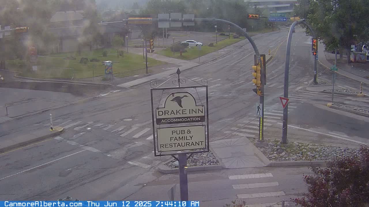 A misty view of a road intersection with traffic signals, a Drake Inn sign, and a few cars, showing a mostly overcast day.