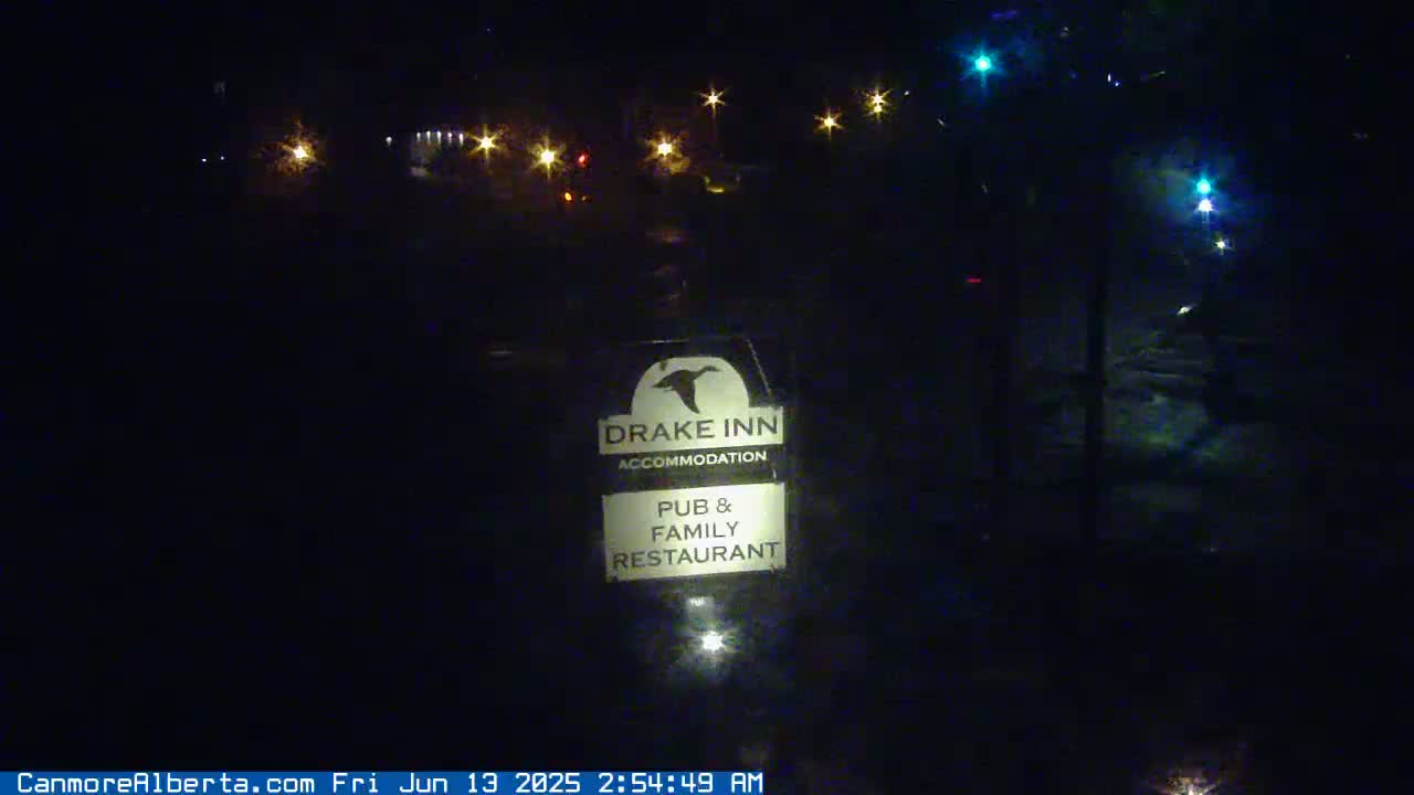 A nighttime view of a Drake Inn sign indicating accommodation, pub, and family restaurant services, with distant streetlights visible in the dark.