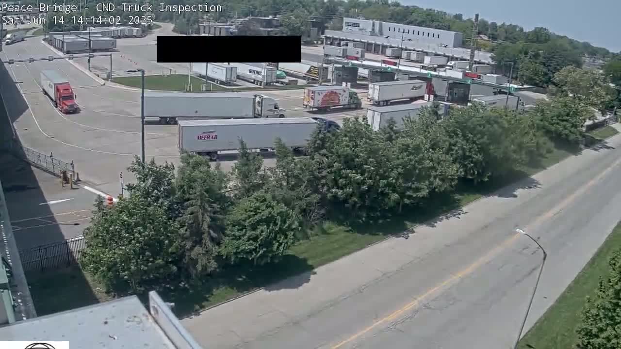 Several semi-trailer trucks are parked and moving around a truck inspection area on a sunny day.