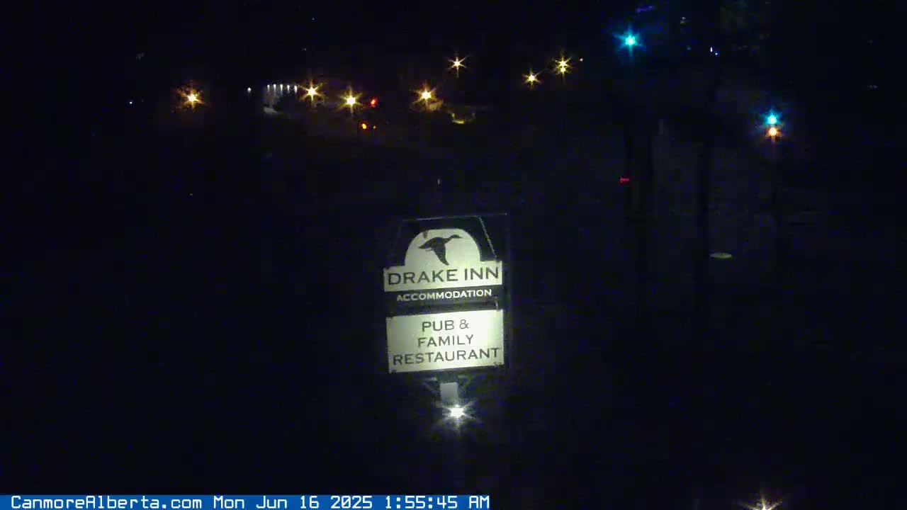A nighttime image shows a Drake Inn sign illuminated in the dark, with distant lights visible in the background under a clear night sky.