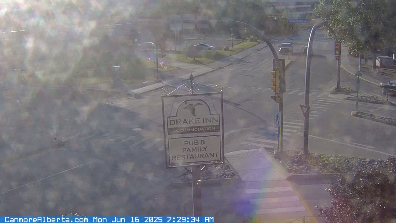 A hazy, sunny morning view of a street intersection with a Drake Inn sign, showing a pub and family restaurant, and a few cars.