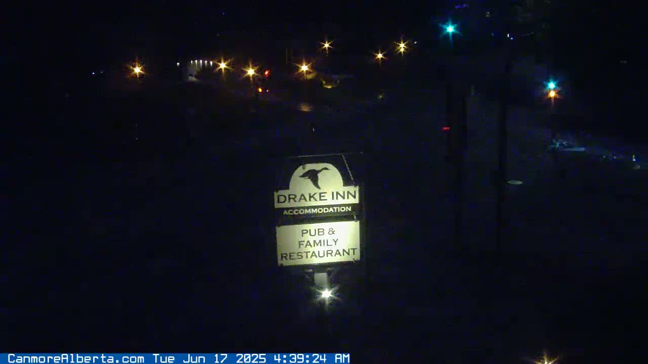 A nighttime view of a Drake Inn sign illuminated in front of a dark road with distant lights.