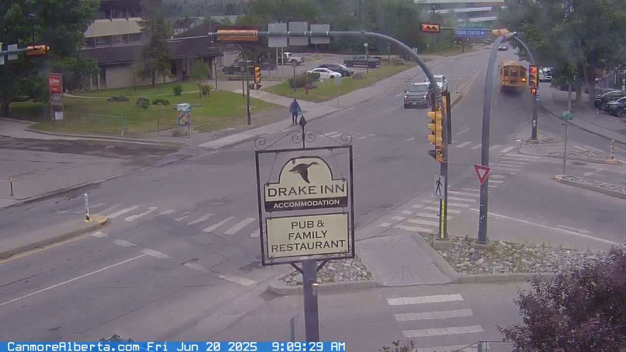 A street intersection with a Drake Inn sign, a school bus, several cars, and a pedestrian, under an overcast sky.