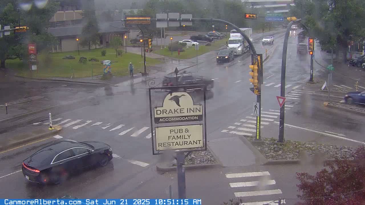 A rainy scene shows a busy intersection with several cars, a pedestrian, and a Drake Inn sign.