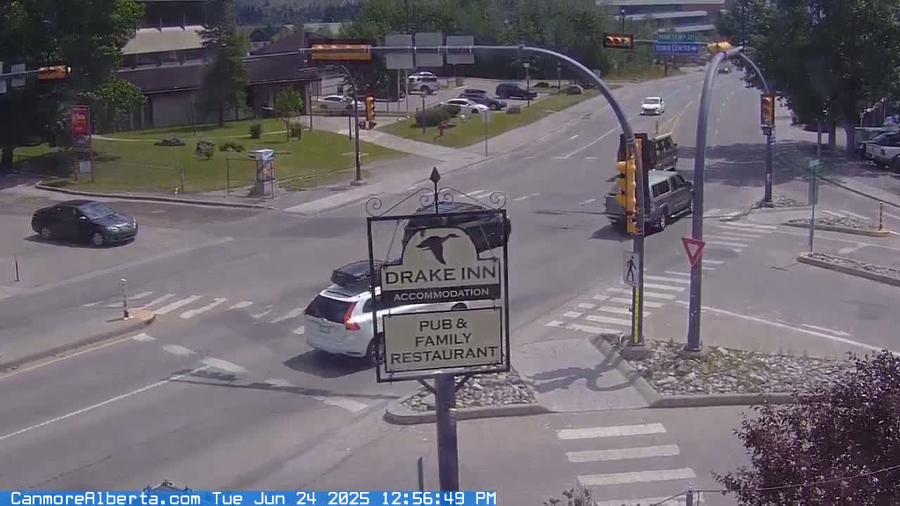 A sunny day shows several vehicles at a crossroads near a Drake Inn sign, with some cars stopped at traffic signals.