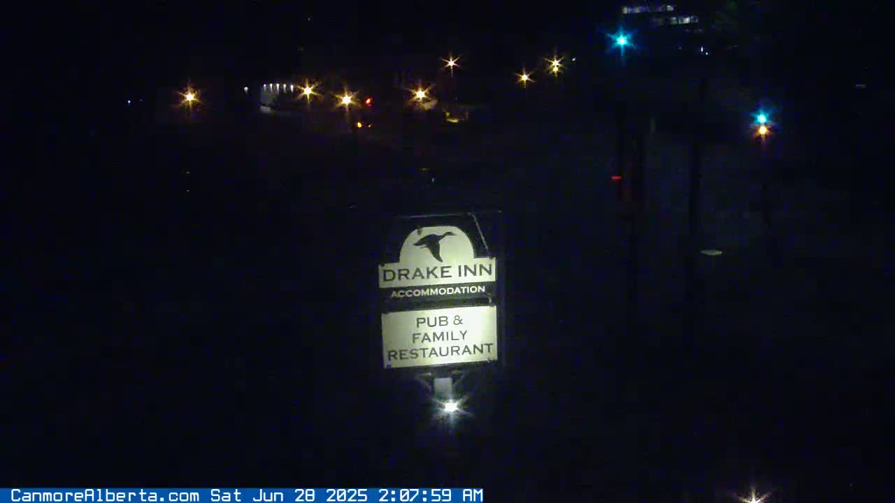 A nighttime view of a Drake Inn sign illuminated by a light source, with several other lights visible in the distance.