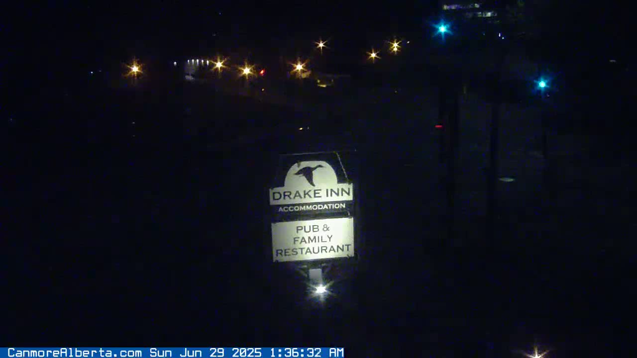 A nighttime view of a Drake Inn sign advertising accommodation, a pub, and a family restaurant, illuminated by distant lights under a clear, dark sky.