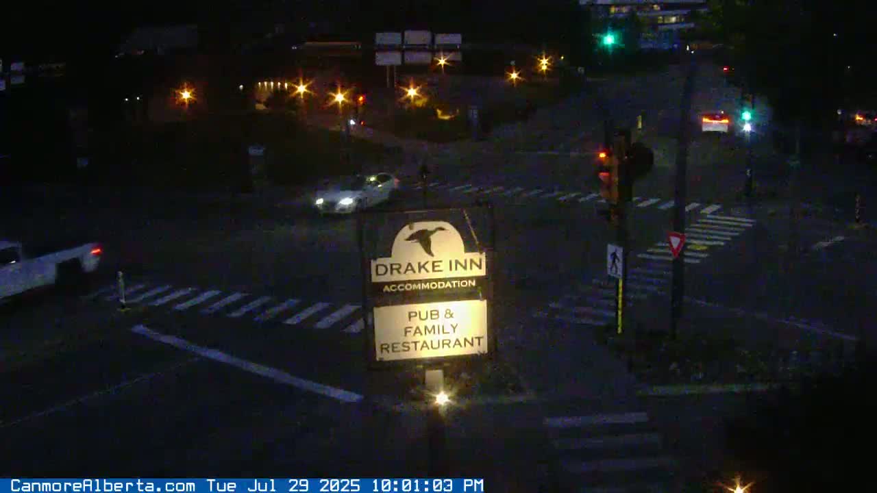 A nighttime, outdoor view of a Drake Inn sign illuminated by a light at its base, with distant lights visible in the background.