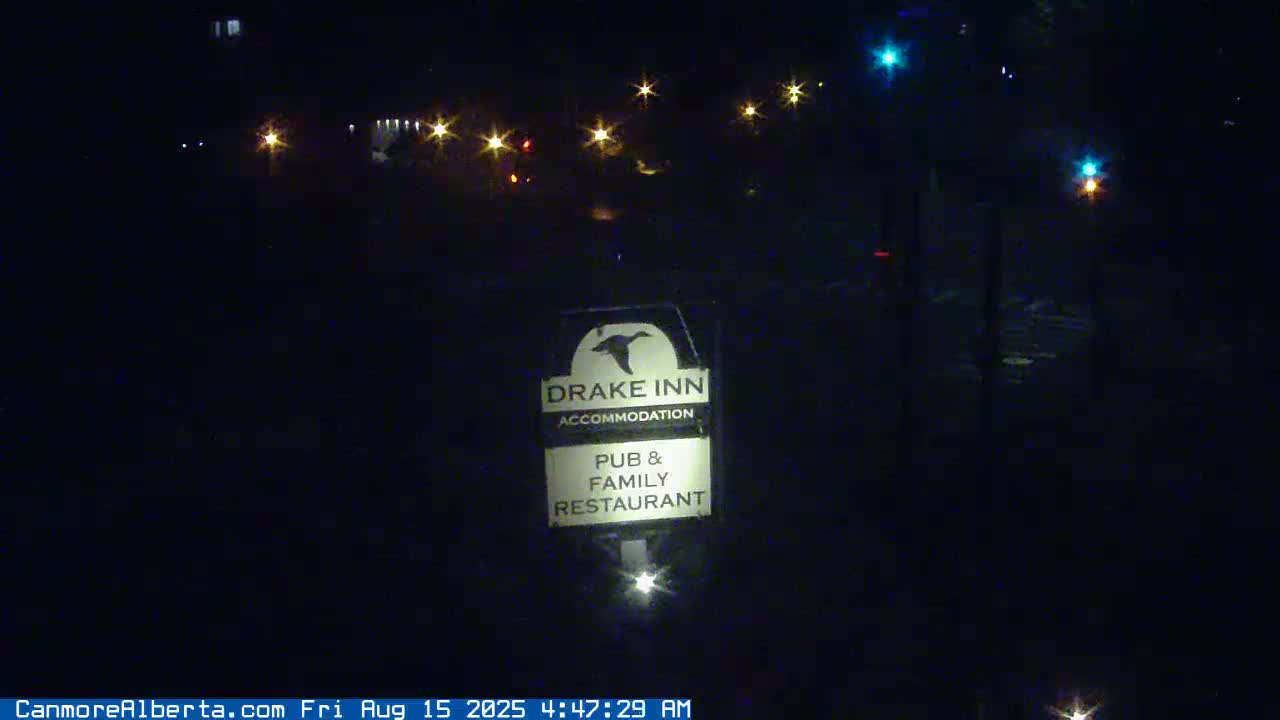 A nighttime, outdoor view of a Drake Inn sign illuminated by a light at its base, with distant lights visible in the background.