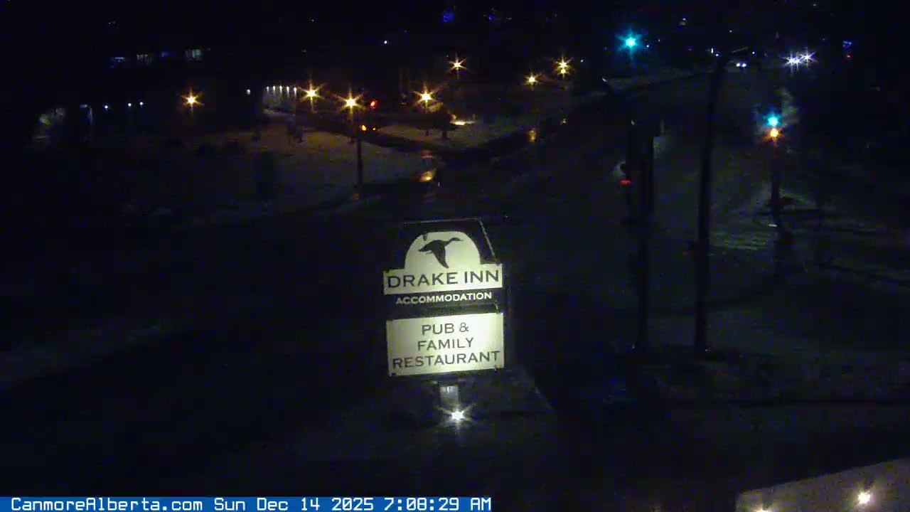 A nighttime, outdoor view of a Drake Inn sign illuminated by a light at its base, with distant lights visible in the background.