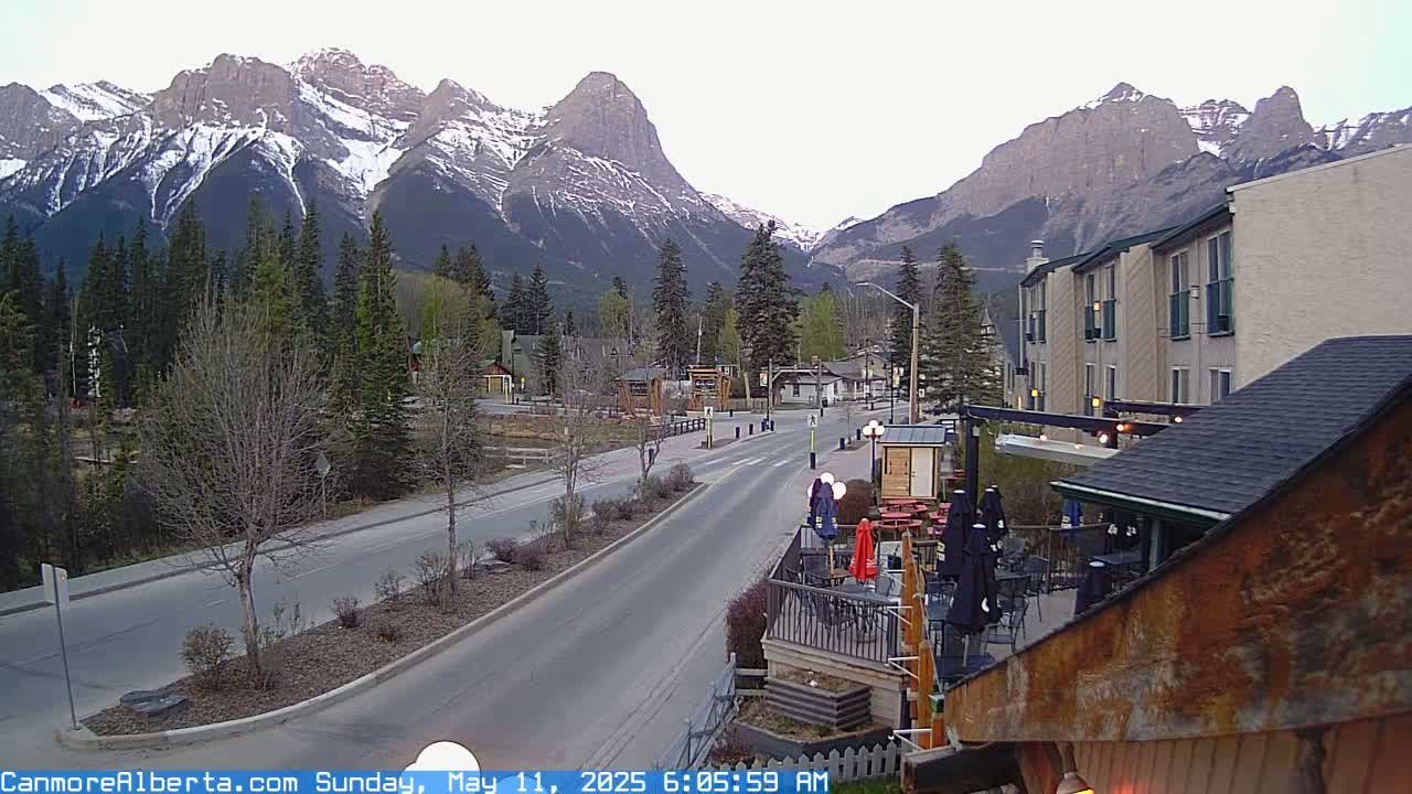 A mostly clear, early morning view of a town nestled in a valley, with snow-capped mountains in the background and a roadway leading toward them.