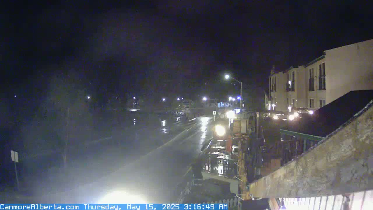 A wet, nighttime street scene shows a roadway with some vehicle lights, and a multi-story building is visible on the right.