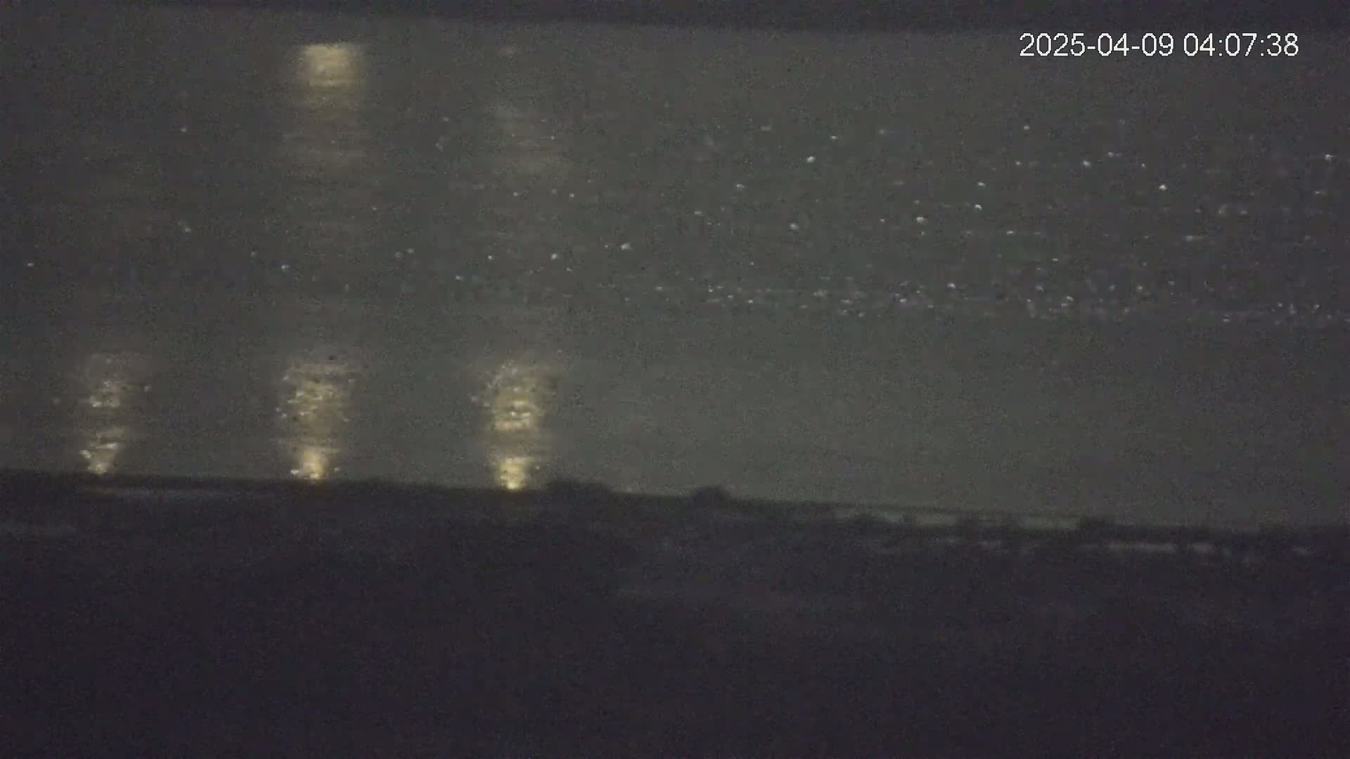 A nighttime view of a dark body of water reflecting lights from the shore under a mostly clear sky.