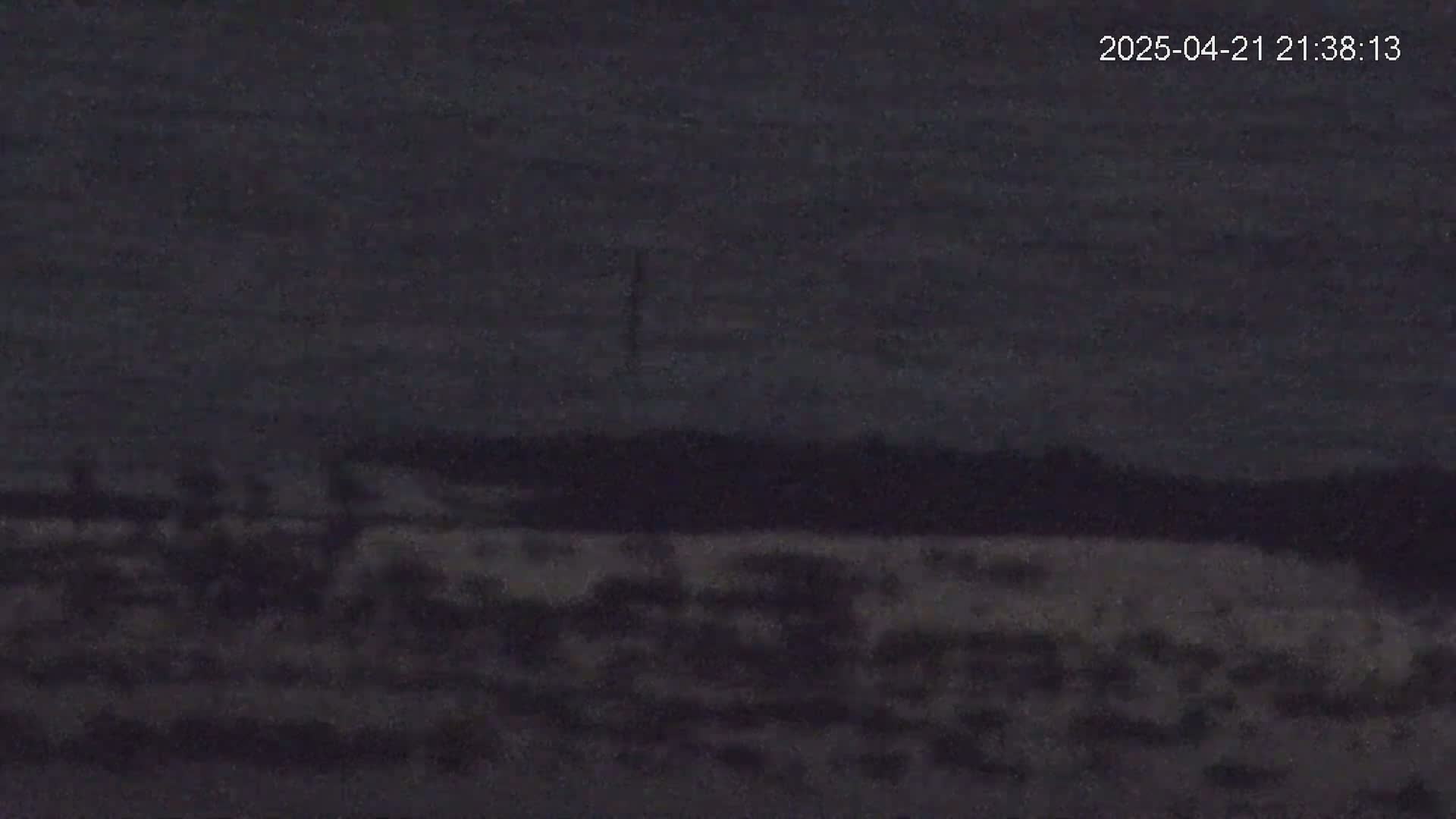 A dark, nighttime landscape shows a flat expanse of land under a cloudy sky.