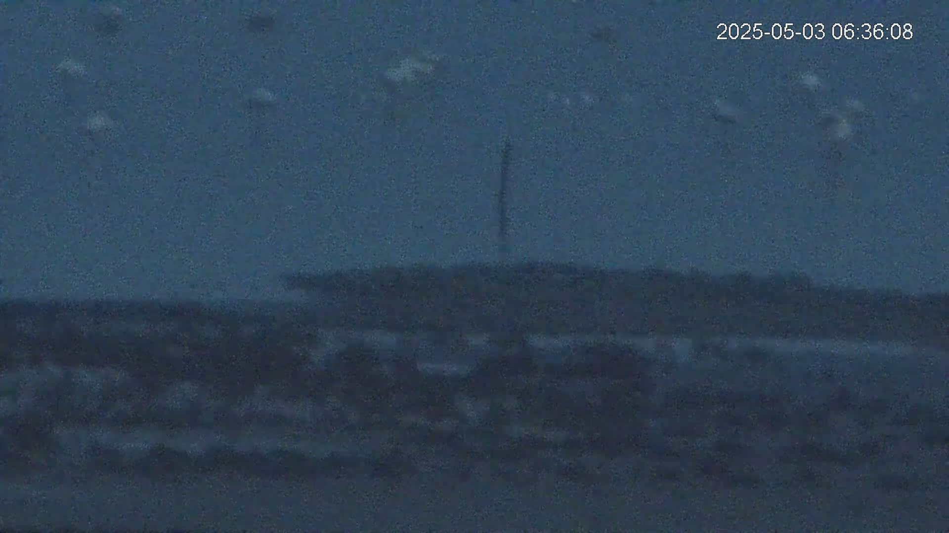 A dark, blurry landscape shows a tall, thin structure in the distance under a dusky sky.