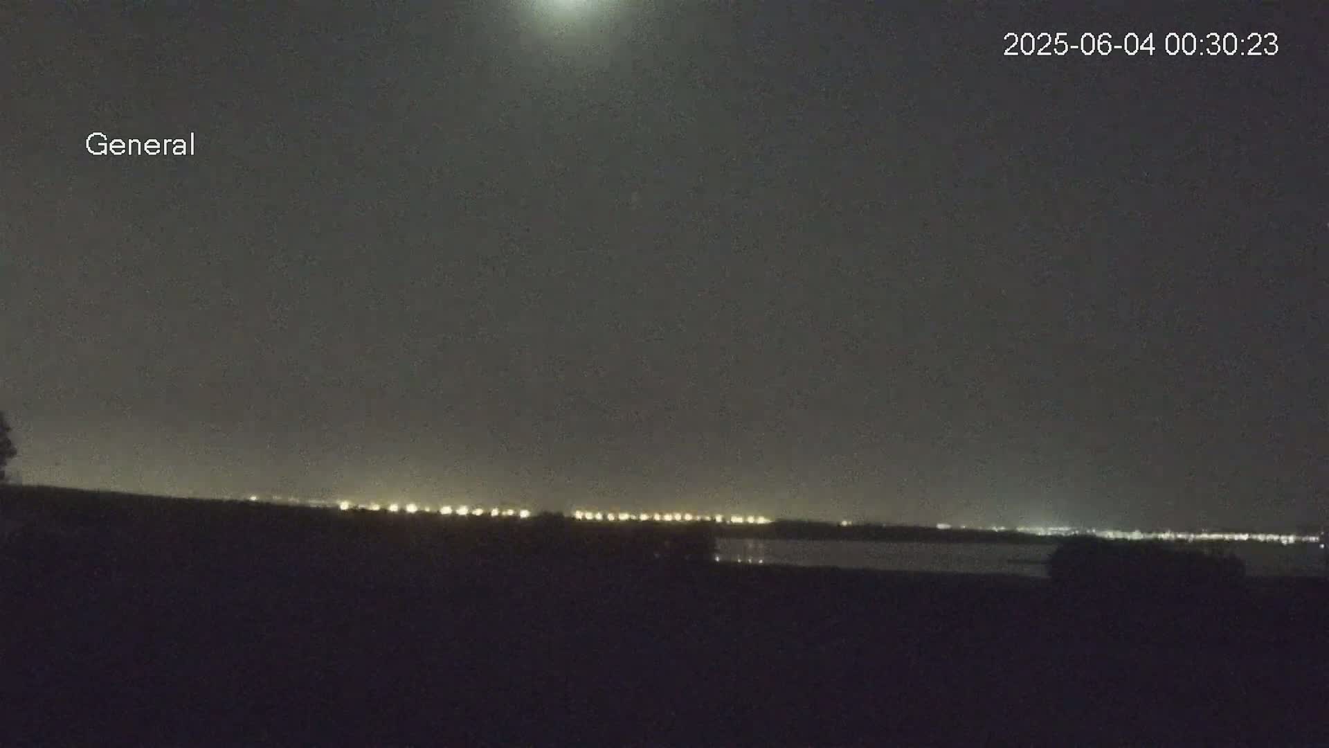 A nighttime long shot shows a line of distant lights on the horizon under a dark, clear sky.