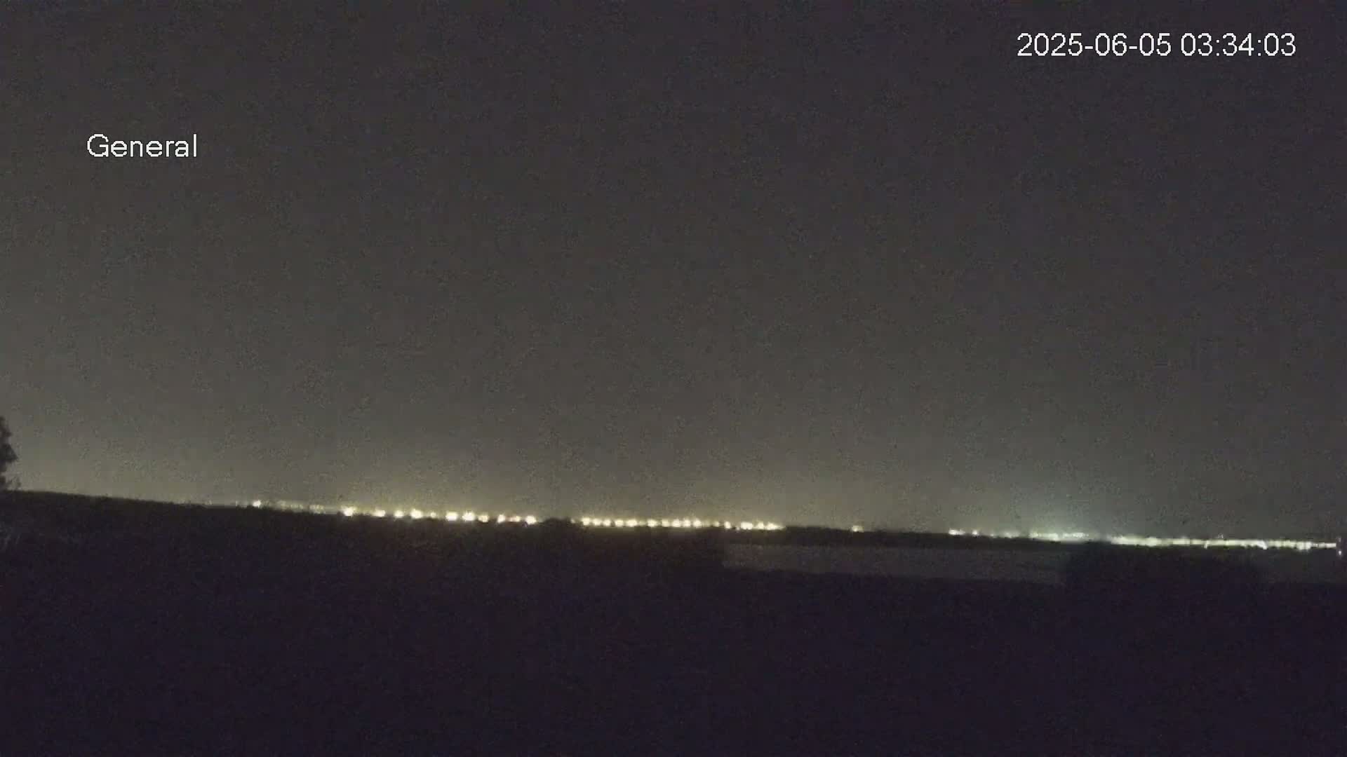 A nighttime, long-range view shows a line of distant lights on the horizon under a dark sky.