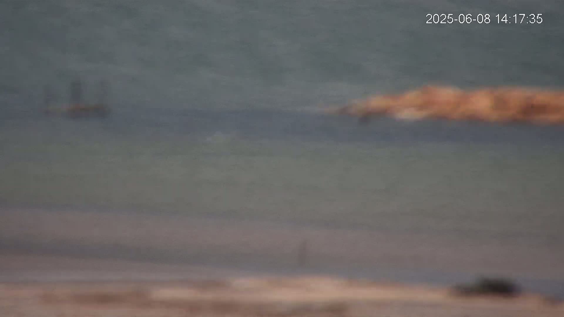 A distant view of a calm body of water with a small, indistinct object on the shore and a larger, blurred object in the water.