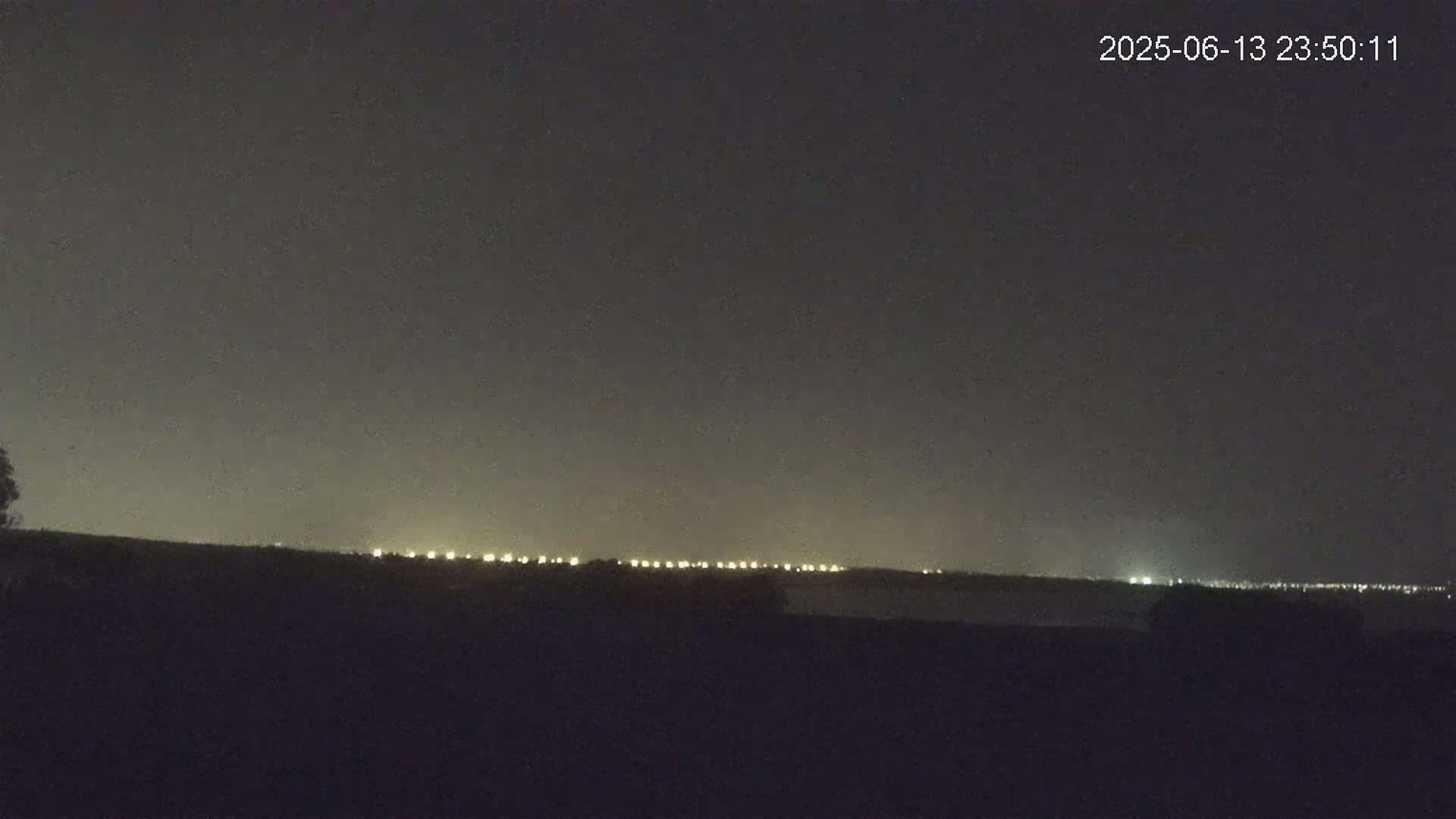 A nighttime, long-range view shows a line of distant lights on the horizon under a dark sky.