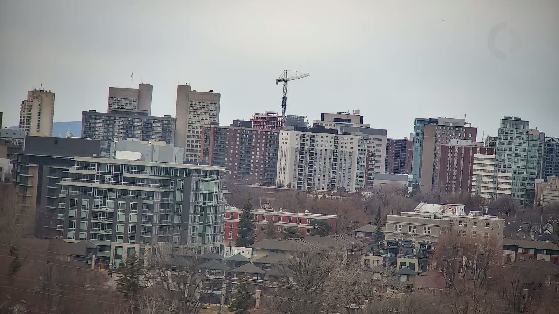 A cityscape of many high-rise apartment buildings and houses under a cloudy sky, with a construction crane visible in the distance.