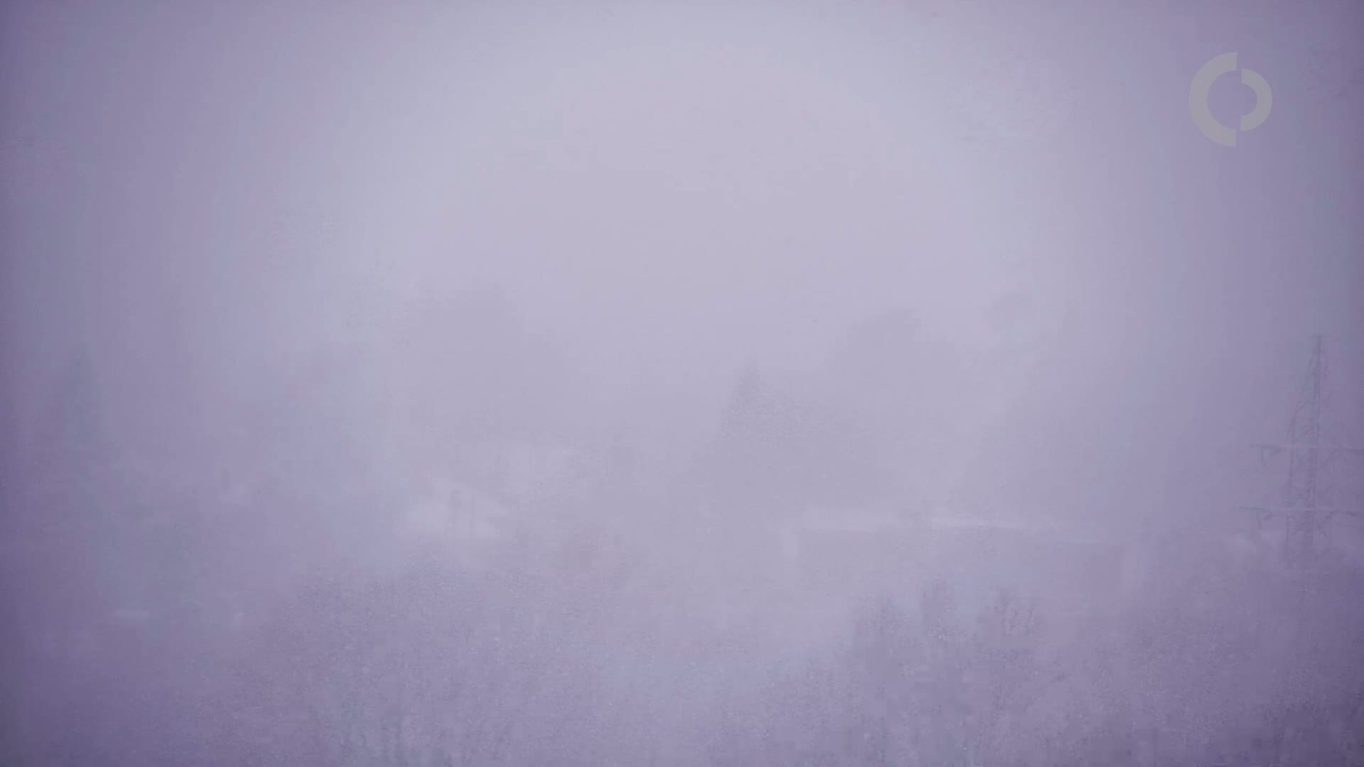 A hazy, snowy landscape is barely visible through a thick fog.
