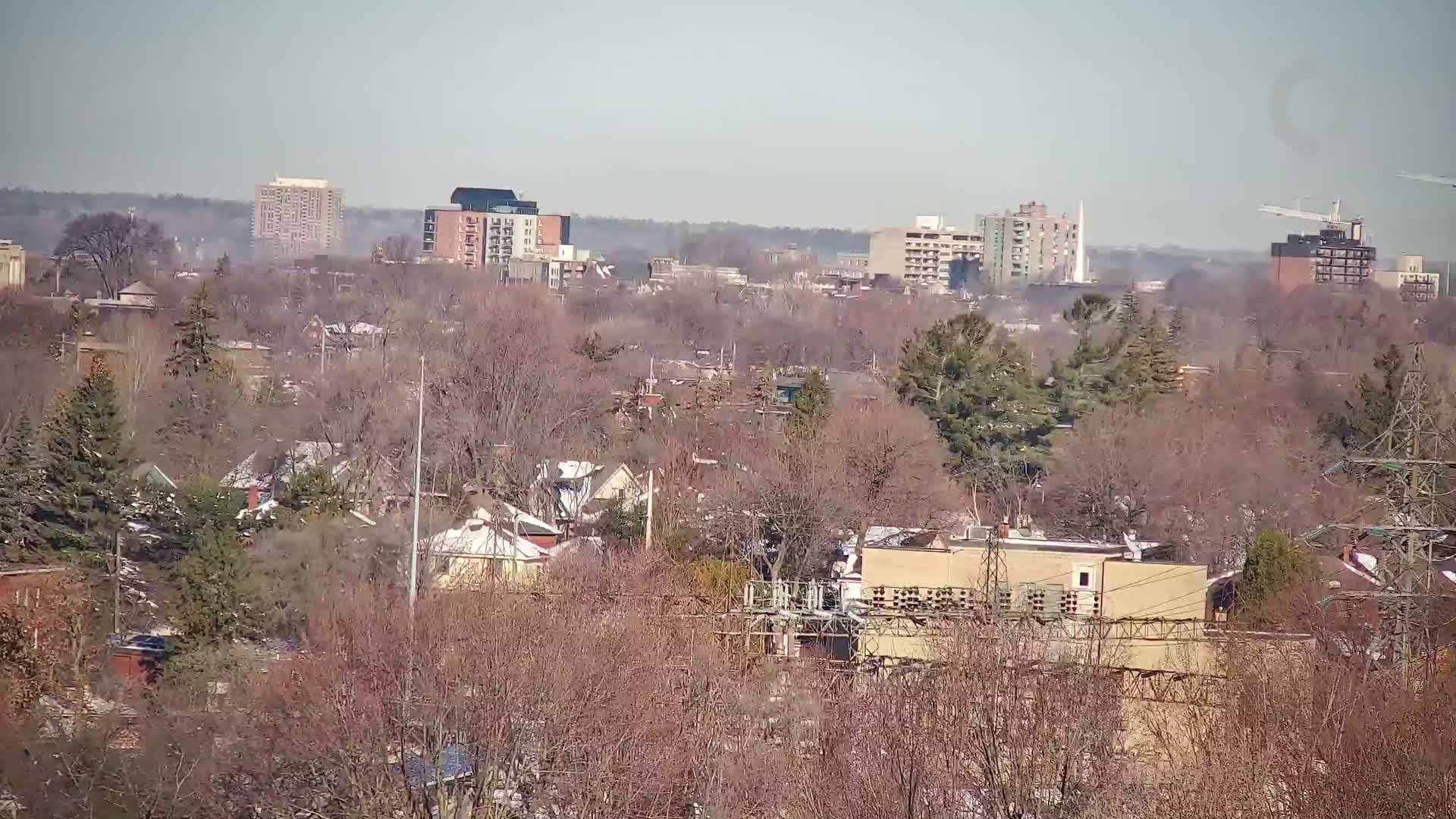 A hazy, sunny day reveals a cityscape of apartment buildings and houses nestled amongst bare, winter trees.