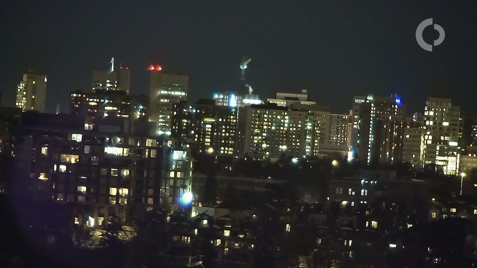A cityscape at night with many buildings illuminated, under a dark sky.