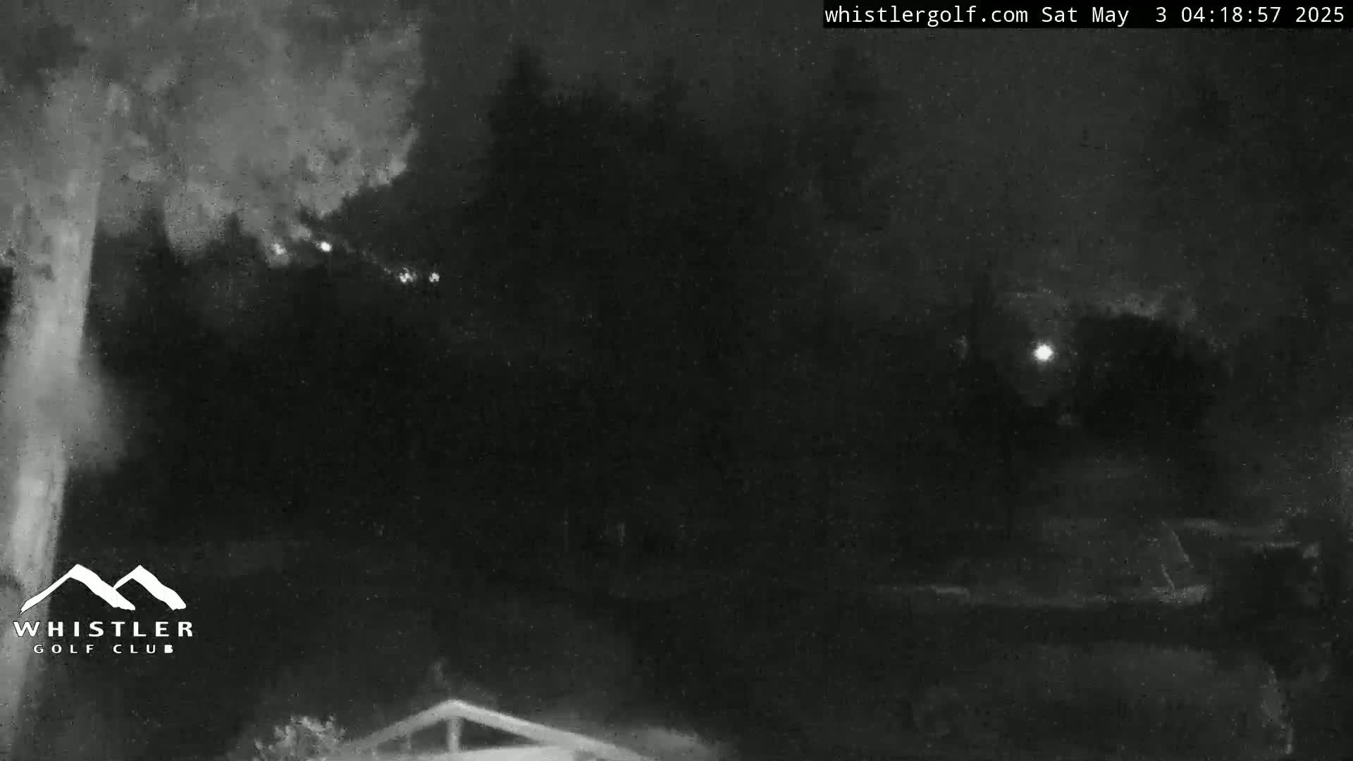 A nighttime, low-light view shows dark trees and a dimly lit area, possibly a golf course, with some distant lights visible.