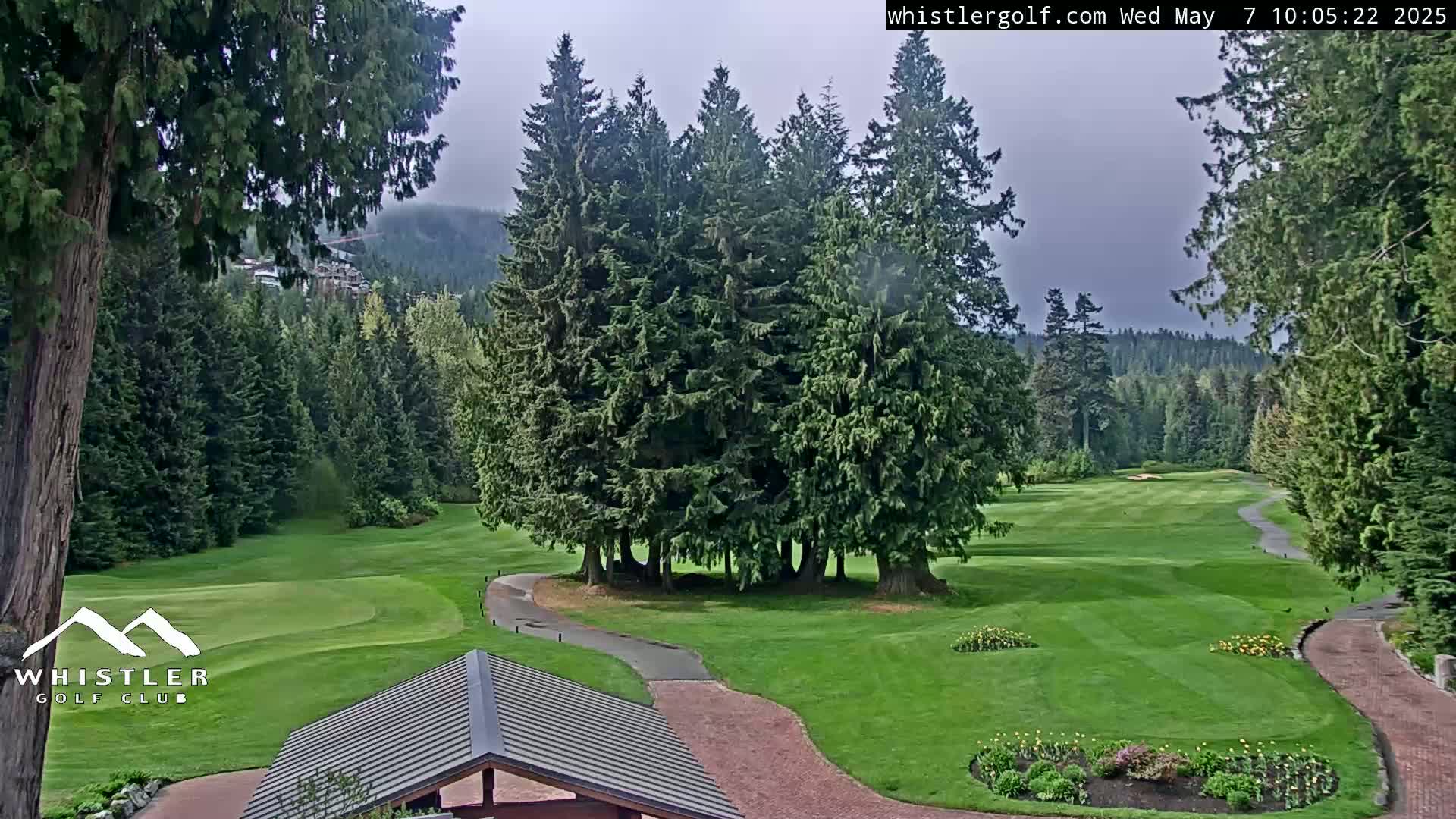 A golf course with a brick path, lush green grass, and evergreen trees under an overcast sky.