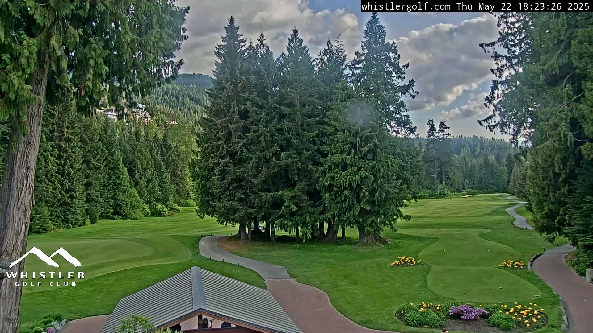 A golf course nestled among evergreen trees under a partly cloudy sky.
