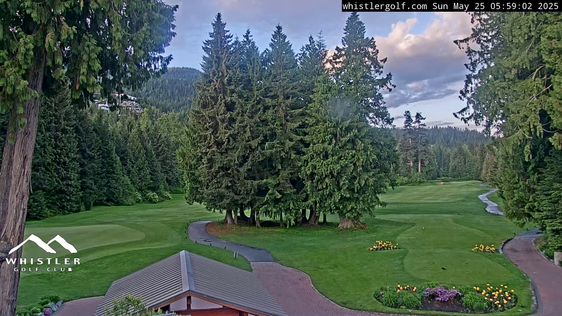 A golf course nestled in a lush green forest under a partly cloudy sky.