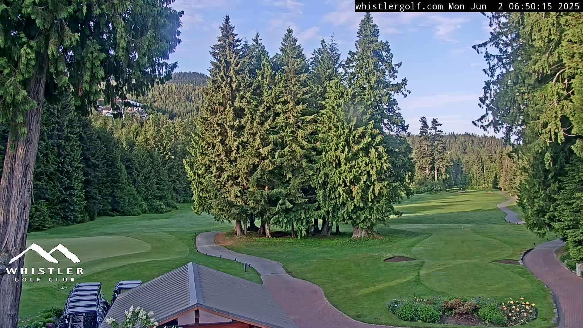 A golf course nestled in a forest of evergreen trees under a partly cloudy sky.