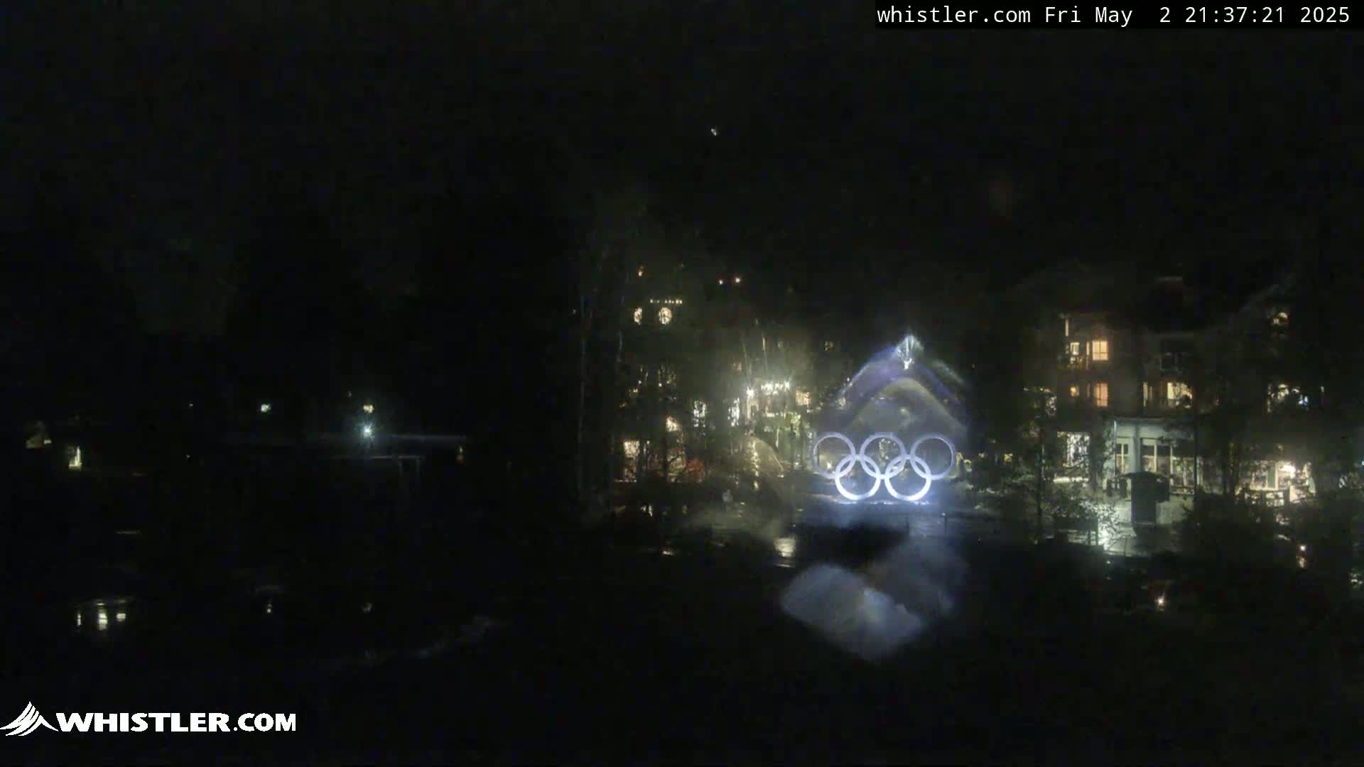 A nighttime view of the Olympic rings illuminated in front of a building complex.