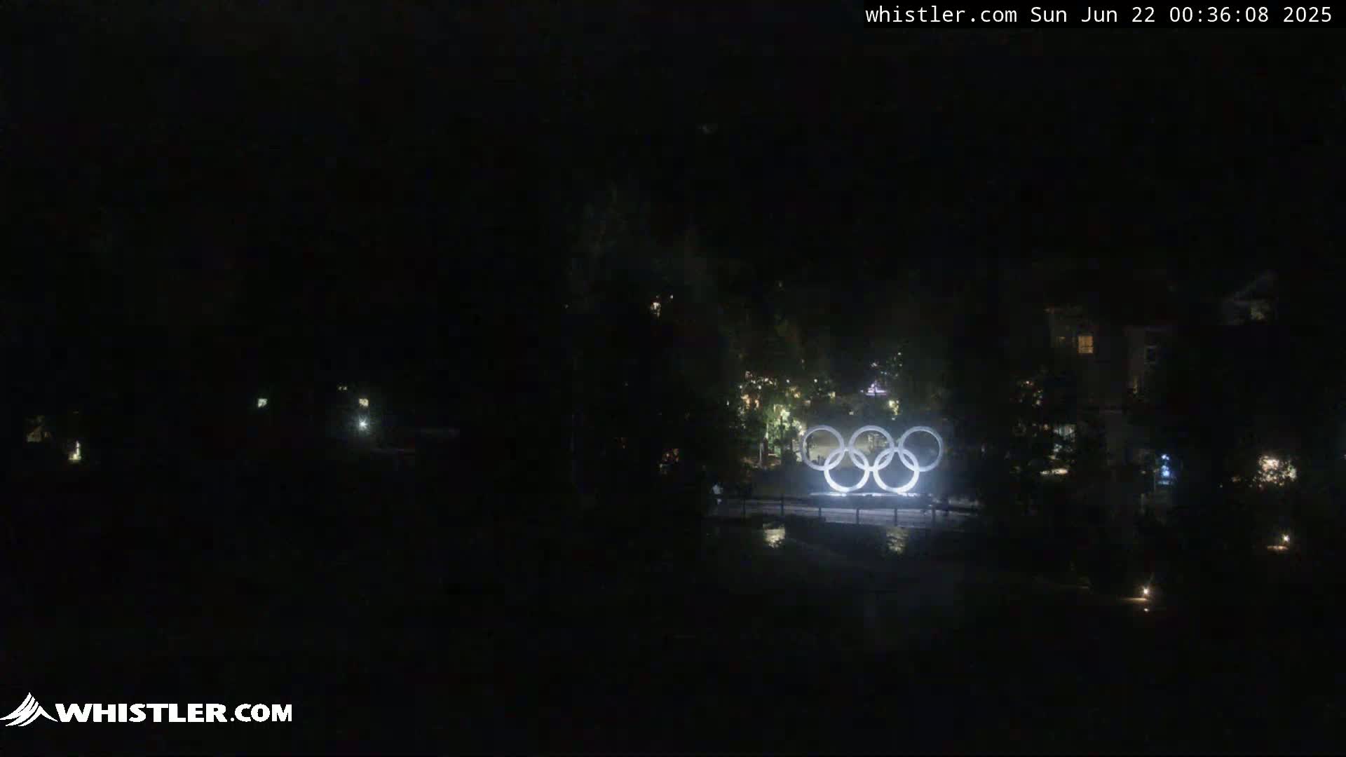 Illuminated Olympic rings are visible at night in a dark, outdoor setting.