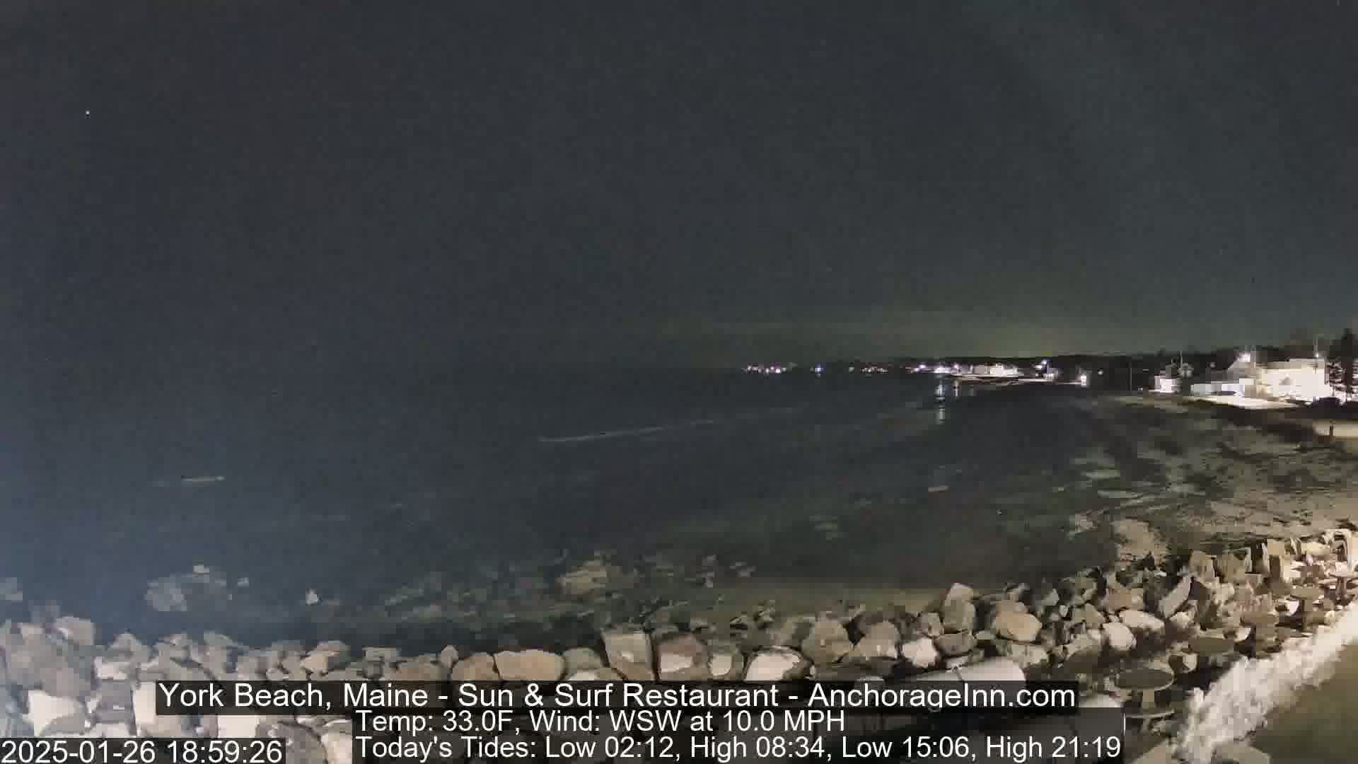 A nighttime view of a rocky shoreline and calm ocean under a dark sky.