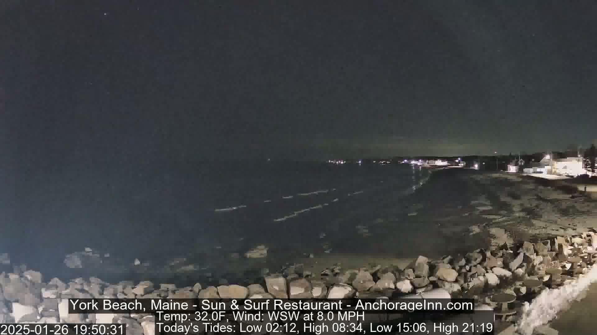 A nighttime view of a rocky shoreline and dark ocean under a clear sky with a slight wind.