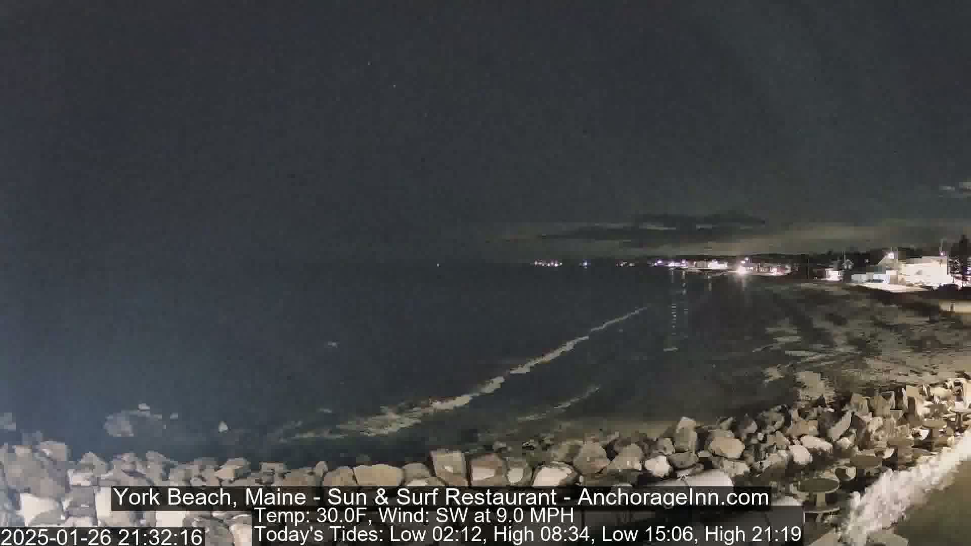 A nighttime view of a rocky shoreline and dark ocean under a clear sky.