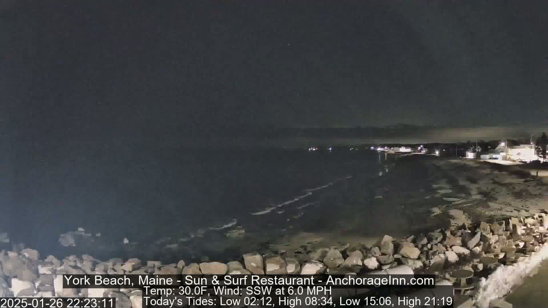 A nighttime view of a rocky shoreline with gently lapping waves under a dark sky, and a 30°F temperature with a 6.0 mph south-southwesterly wind.