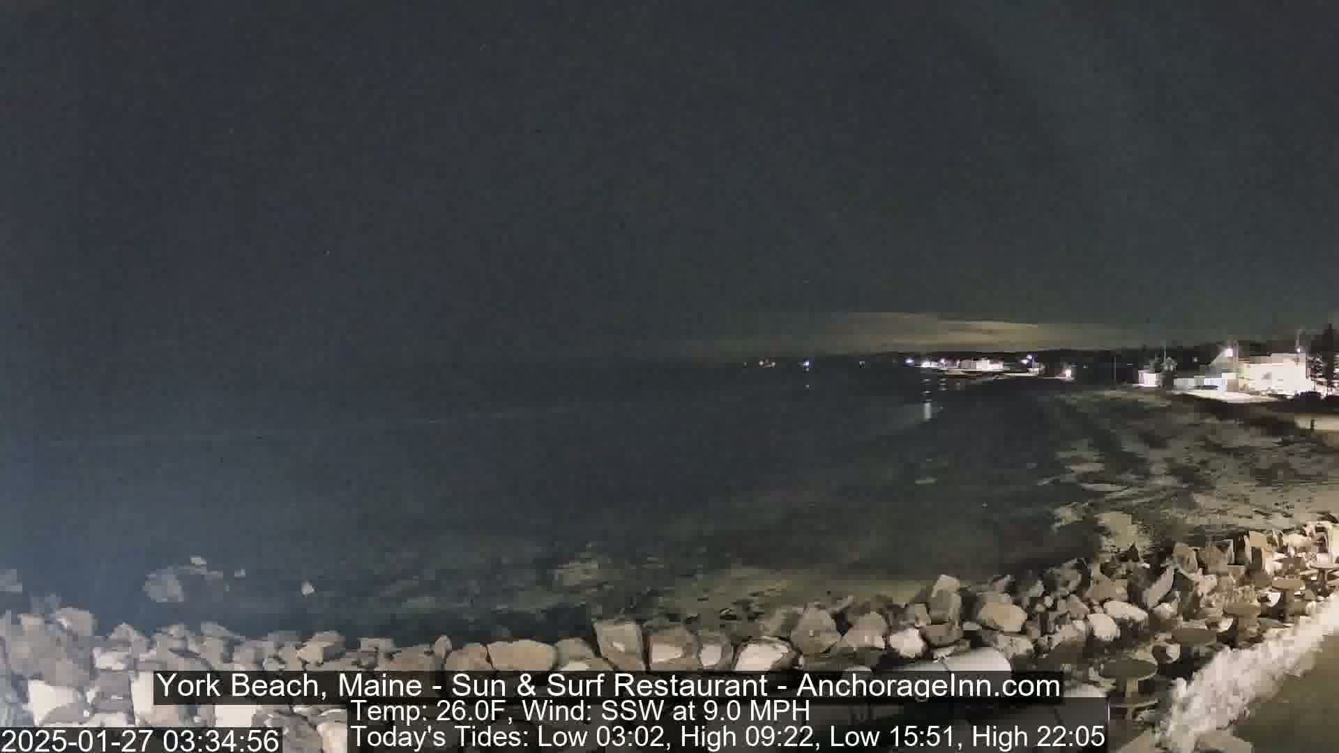 A nighttime view of a rocky shoreline and dark ocean under a mostly clear sky.